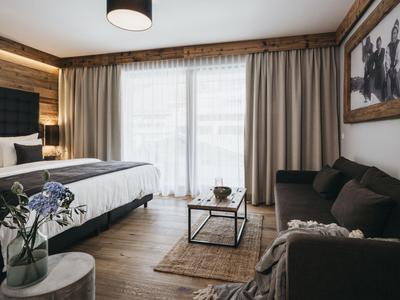 Hell gestaltetes Hotelzimmer mit großem Bett, Sofa und Fenster mit Vorhängen.