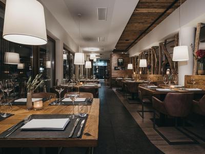 Elegantes Restaurantinterieur mit Holztischen, Ledersesseln und gedämpfter Beleuchtung.