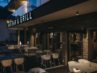 Außenbereich einer Bar und Grill mit modernen Tischen und Stühlen, beleuchtet in der Dämmerung.