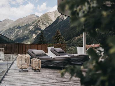 Zwei Liegen auf einer Terrasse mit Bergblick und Wolkenhimmel im Hintergrund.
