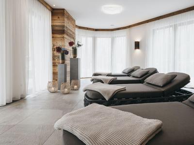 Modernes Hotelzimmer mit großen Fenstern, hellen Vorhängen und mehreren gemütlichen Liegen.