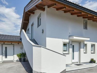 Modernes, weißes Ferienhaus mit Holzgiebel, großen Fenstern und klarem Himmel.