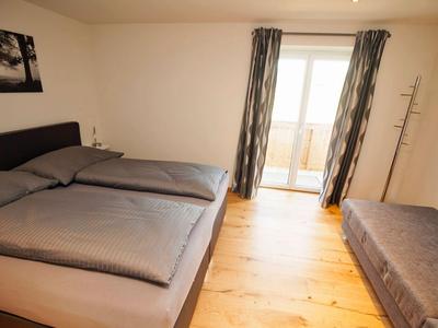 Helles Hotelzimmer mit Doppelbett, Holzfußboden und Balkonzugang durch Glasschiebetür.