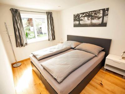 Helles Schlafzimmer mit Doppelbett, Nachttisch und Fenster mit Vorhängen in einem Hotel.