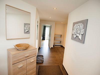 Heller Flur mit Holzkommode, Spiegel und Bild an den weißen Wänden in einem Hotelzimmer.