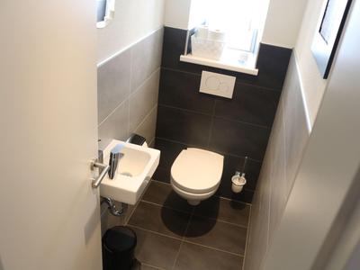 Kleines, modernes Hotel-WC mit weißer Toilette, kleinem Waschbecken und grauen Fliesen.