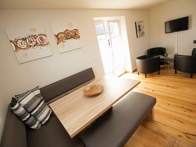Helles Zimmer mit Holzboden, Esstisch, Sitzbank, Sesseln und Wandbildern im Hotel.