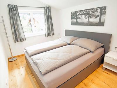 Helles Schlafzimmer mit Doppelbett, Holzboden und Fenster mit grauen Vorhängen.