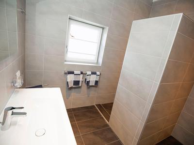 Modernes Badezimmer mit großer Dusche und weißem Waschbecken in warmen Brauntönen.