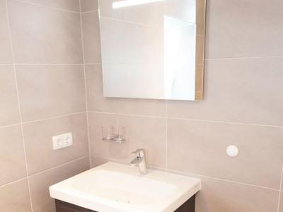 Kleiner Hotelbadezimmer-Waschbecken mit Spiegel, Wasserhahn und hellen Wandfliesen.