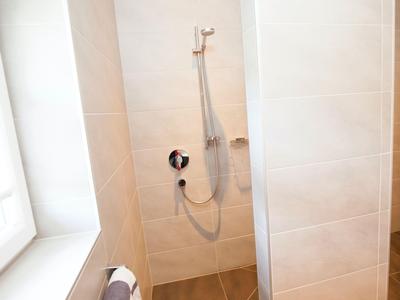 Moderne Duschkabine mit großen weißen Fliesen und Handbrause im Hotelbad.
