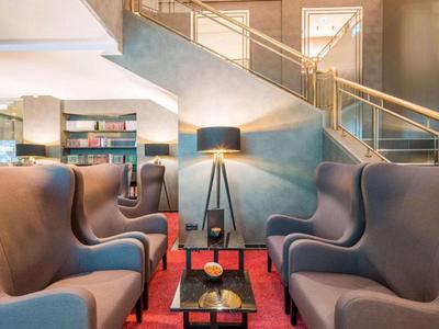 Modern hotel lounge with comfortable armchairs and a floor lamp near stairs.