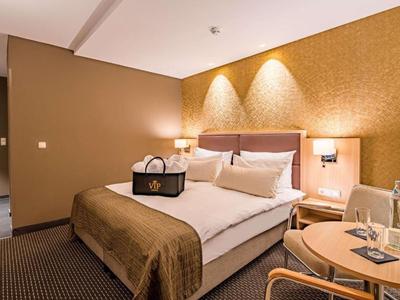 Modernly furnished hotel room with double bed, warm colors, and a small table.
