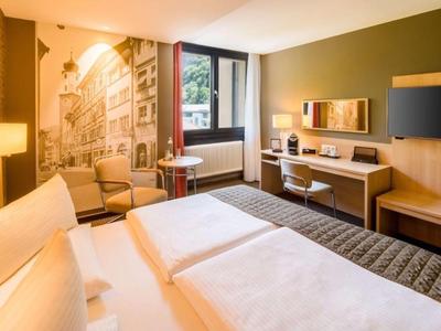 Modern hotel room with two beds, desk, and cityscape wall art.