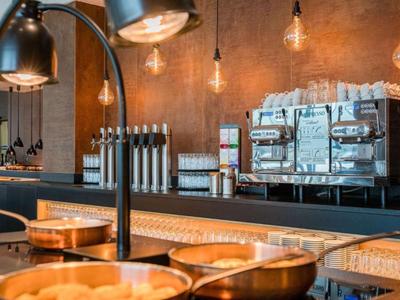Modern hotel bar with copper details, hanging lights, and multiple coffee machines.