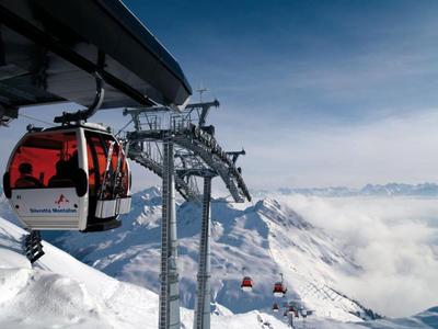 Red cable car over snowy mountains with blue sky and clouds.