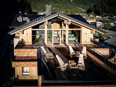 Chalet moderne avec grande terrasse en bois et mobilier d’extérieur dans un cadre montagneux en plein soleil.