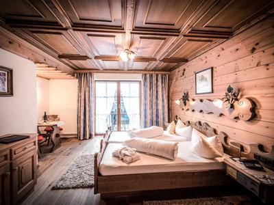 Chambre d'hôtel confortable avec murs en bois, grand lit, tapis et balcon avec vue sur la montagne.