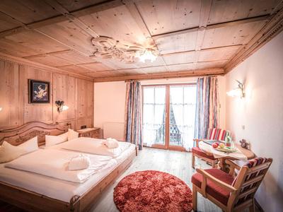 Chambre d'hôtel confortable avec mobilier en bois, lit double, coin salon et balcon.