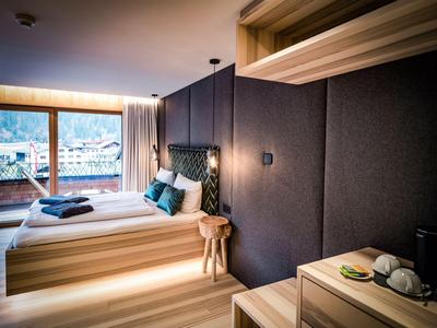 Chambre d'hôtel moderne avec lit double, éléments en bois et vue sur la montagne à travers de grandes fenêtres.