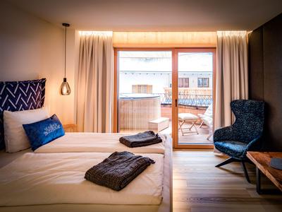 Chambre d'hôtel confortable avec lit double, fauteuil et balcon avec mobilier en bois.