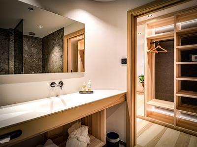 Salle de bain lumineuse avec grand miroir, plan de travail blanc et dressing attenant.