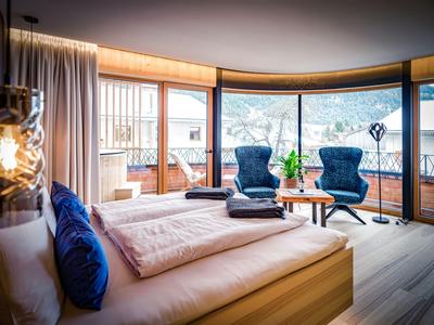 Chambre d'hôtel moderne avec fenêtres panoramiques, deux fauteuils et balcon offrant une vue sur la montagne.
