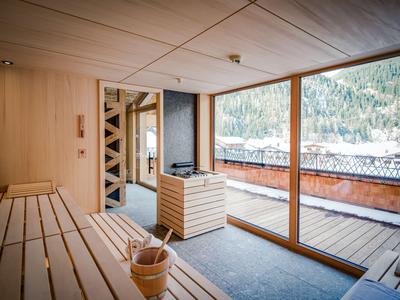 Salle de sauna moderne avec bancs en bois, poêle et grande fenêtre sur les montagnes.