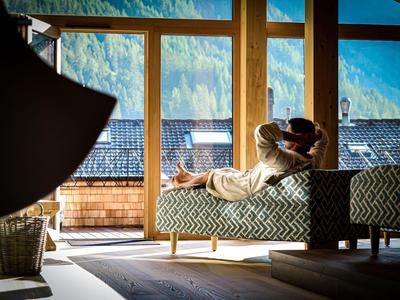 Une personne se détend sur un canapé moderne devant de grandes fenêtres avec vue sur les montagnes dans une chambre d'hôtel.