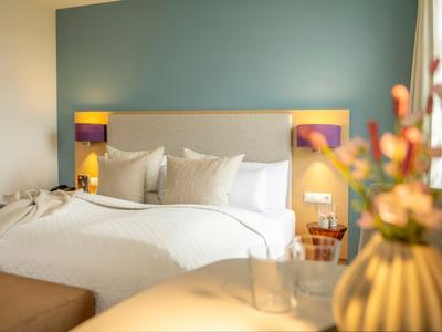 Gemütliches Hotelzimmer mit großem Bett, grüner Wand und dekorativer Blumenvase.