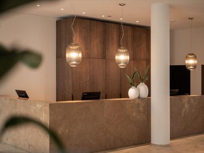 Moderne Hotelrezeption mit Naturstein-Tresen, zwei Hängeleuchten und minimalistischer Dekoration.