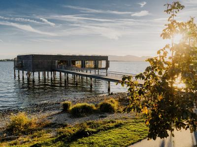 Ein Hotel auf Stelzen über dem Wasser bei Sonnenuntergang mit angrenzendem Holzsteg und Bäumen.