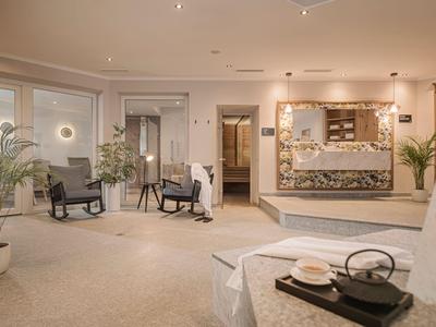 Eleganter Hotel-Loungebereich mit Sessel, Pflanzen und beleuchtetem Empfangstresen in warmem Licht.