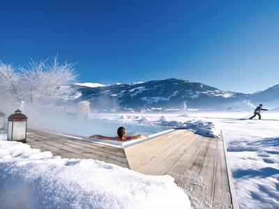 Person entspannt sich im beheizten Außenpool mit Bergblick im verschneiten Winter.