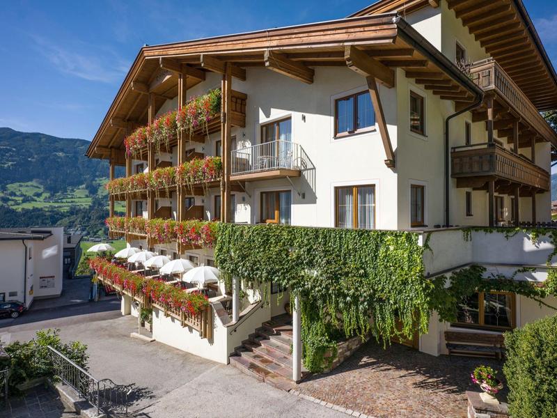 Hotel su più piani con balconi in legno e fiori in stile alpino in una giornata di sole.