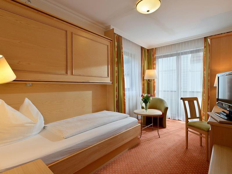 Camera d'hotel accogliente con letto singolo, scrivania, poltrona e finestra con tende.