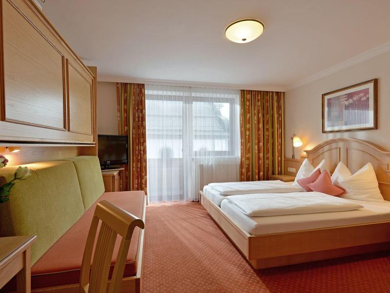 Camera d'hotel accogliente con letto matrimoniale, zona salotto e grande finestra con tende.