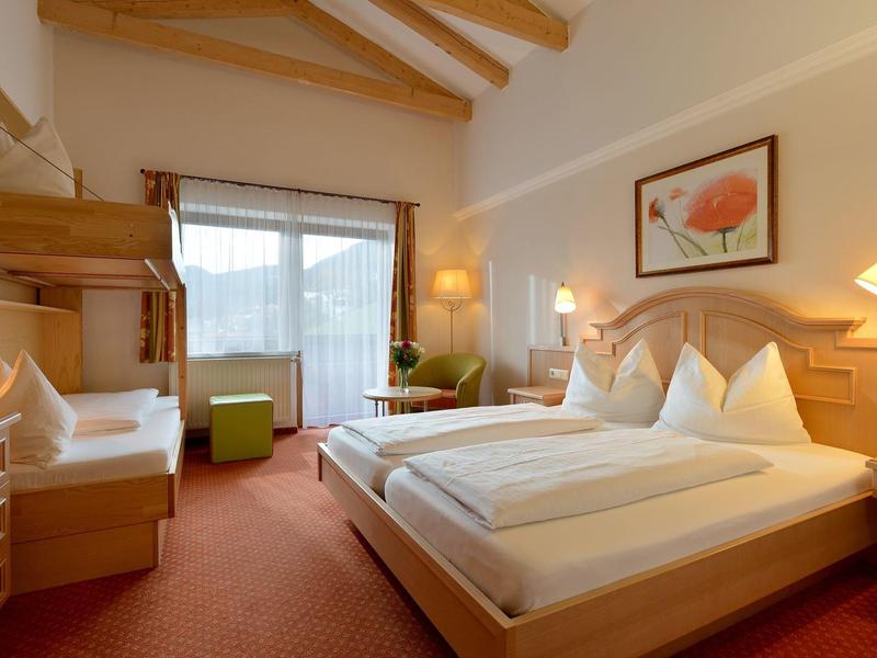 Camera d'hotel luminosa con mobili in legno, letto matrimoniale e zona salotto vicino alla finestra.