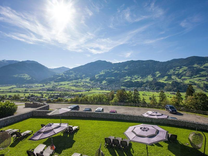 Vista sulle montagne verdi e sulla valle da una terrazza di hotel con ombrelloni e sdraio.