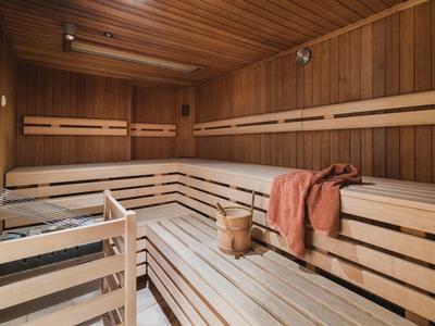 Wooden sauna with benches, a wooden bucket, and a towel draped over a bench.
