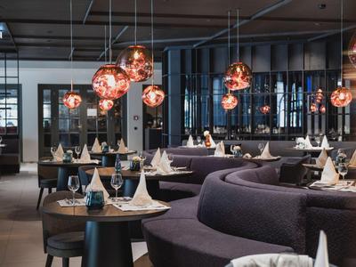 Modern restaurant met ronde zitgedeeltes, elegant gedekte tafels en warme hanglampen.