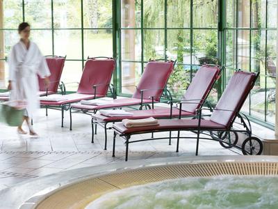Bright indoor pool area with several red loungers and a person in a white bathrobe.