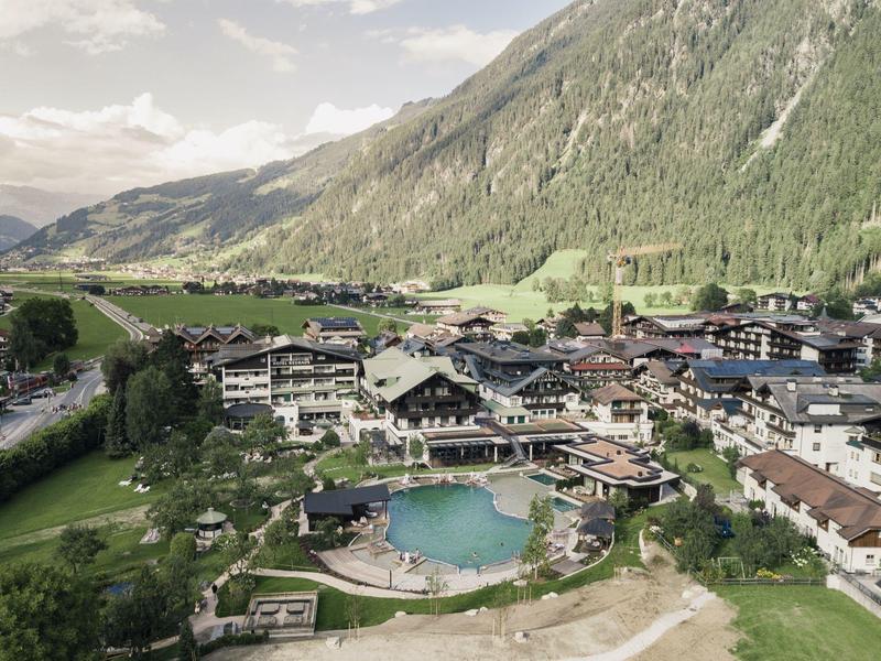 Mountain village with hotels and pool surrounded by green hills and mountains under cloudy sky