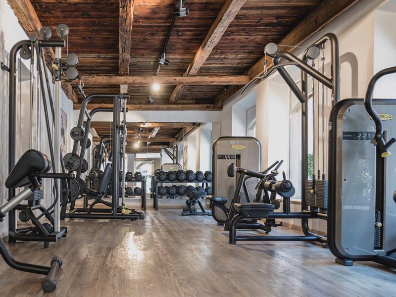 Modern gym with various workout machines and wooden beam ceiling in a hotel.