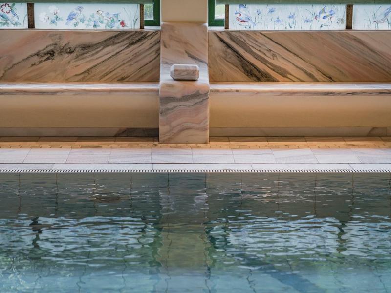 Close-up of a pool water surface with marble cladding and floral windows in the background