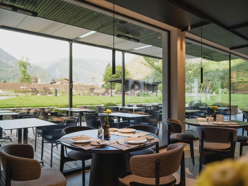 Modern dining area with large windows overlooking green landscape and mountains.