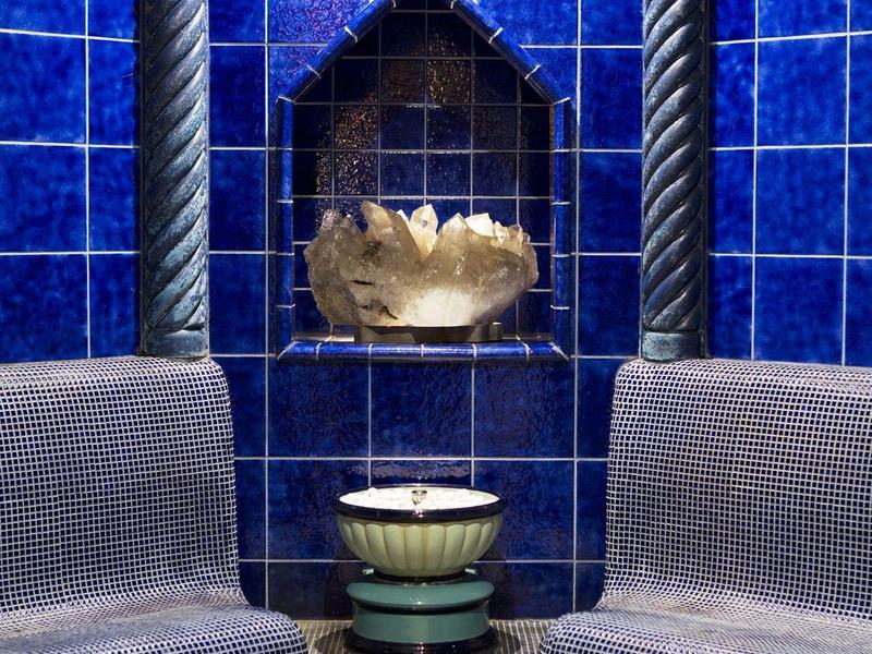 Corner bench with gray cushions against a blue tiled wall and decorative water basin.