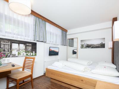 Helles Hotelzimmer mit Doppelbett, Schreibtisch und großem Fenster mit Blick ins Grüne.