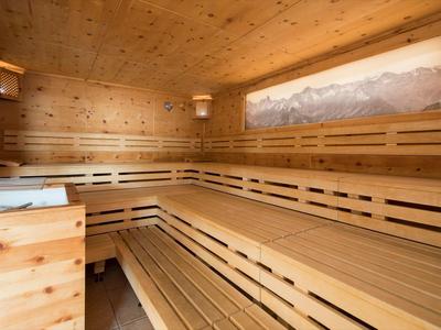 Svítivá sauna s dřevěnými lavicemi a velkým panoramatickým oknem s výhledem na hory.