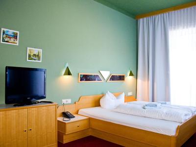 Modernes Hotelzimmer mit Doppelbett, Fernseher und hellem Vorhang am Fenster.